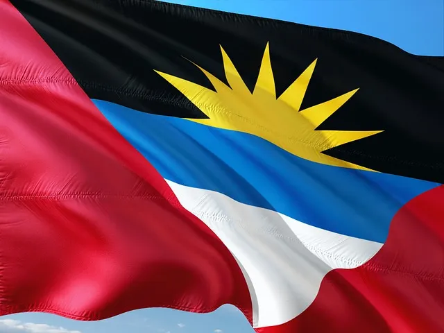 Le drapeau d’Antigua-et-Barbuda flottant sur fond de ciel bleu, avec son soleil doré, ses bandes rouges, noires, bleues et blanches symbolisant l’espoir, la force et la mer des Caraïbes.
