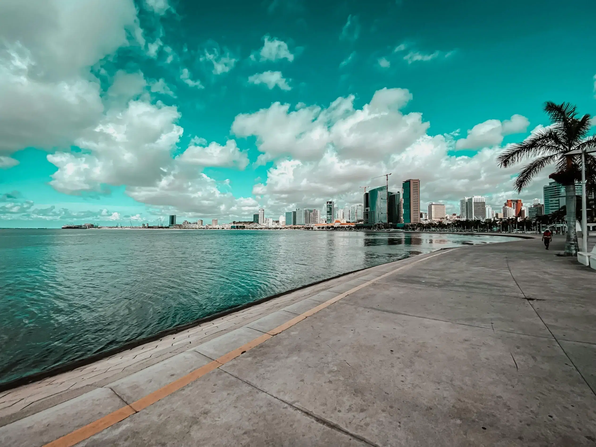 Promenade en bord de mer à Luanda, capitale de l’Angola, avec vue sur les gratte-ciels modernes sous un ciel nuageux et lumineux.
