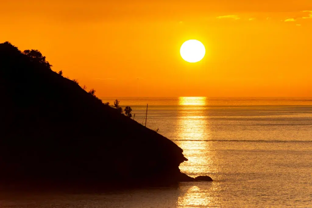 Coucher de soleil flamboyant sur la mer des Caraïbes près de Saint John’s, capitale d’Antigua-et-Barbuda, avec une falaise en silhouette plongeant dans l’eau dorée.