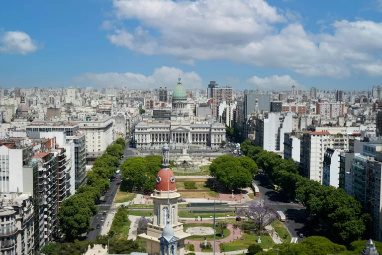 Vue aérienne du centre de Buenos Aires, capitale de l’Argentine, avec le Palais du Congrès national, ses avenues arborées et les immeubles environnants sous un ciel bleu partiellement nuageux.