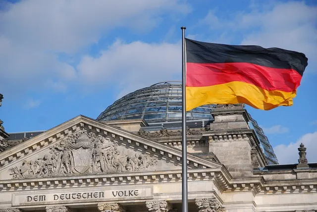 Le drapeau de l’Allemagne flottant devant le bâtiment du Parlement à Berlin, avec l'inscription « Dem Deutschen Volke » visible sur la façade du Reichstag