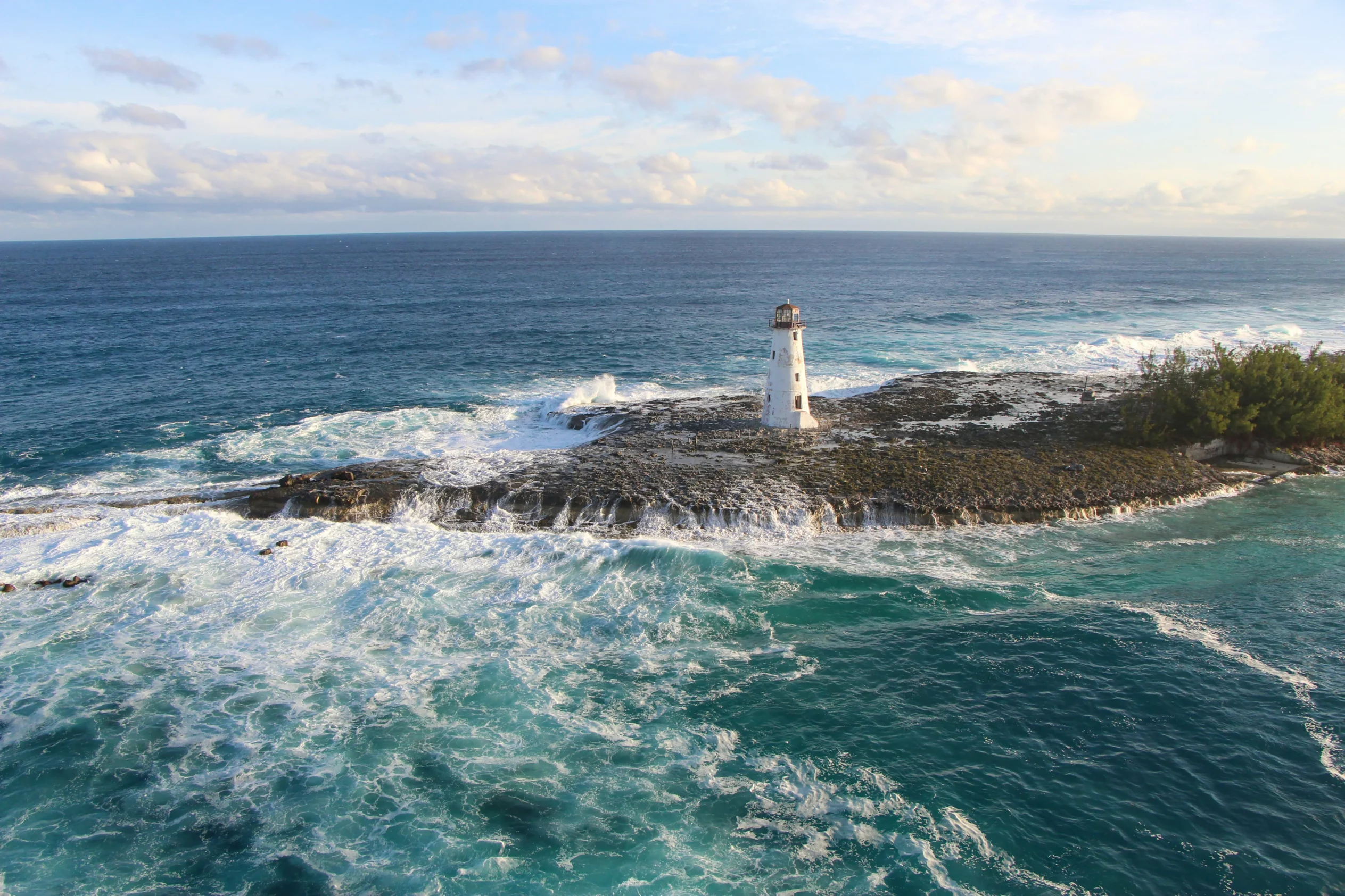 Phare sur une île rocheuse aux Bahamas entouré de vagues puissantes, illustrant la saison humide moins favorable pour partir aux Bahamas.