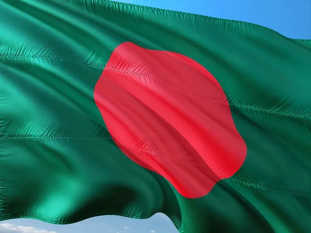 Drapeau vert du Bangladesh avec un cercle rouge légèrement décentré flottant sur fond de ciel bleu.