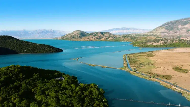 Panorama d’un lac en Albanie sous un ciel bleu dégagé — météo typique d’un été ensoleillé et chaud.
