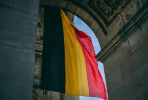 Drapeau de la Belgique flottant sous une arche en pierre, avec ses trois bandes verticales noire, jaune et rouge.