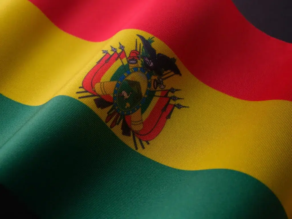 Gros plan sur le drapeau de la Bolivie aux couleurs rouge, jaune et vert avec les armoiries nationales, symbole fort de l’identité bolivienne.