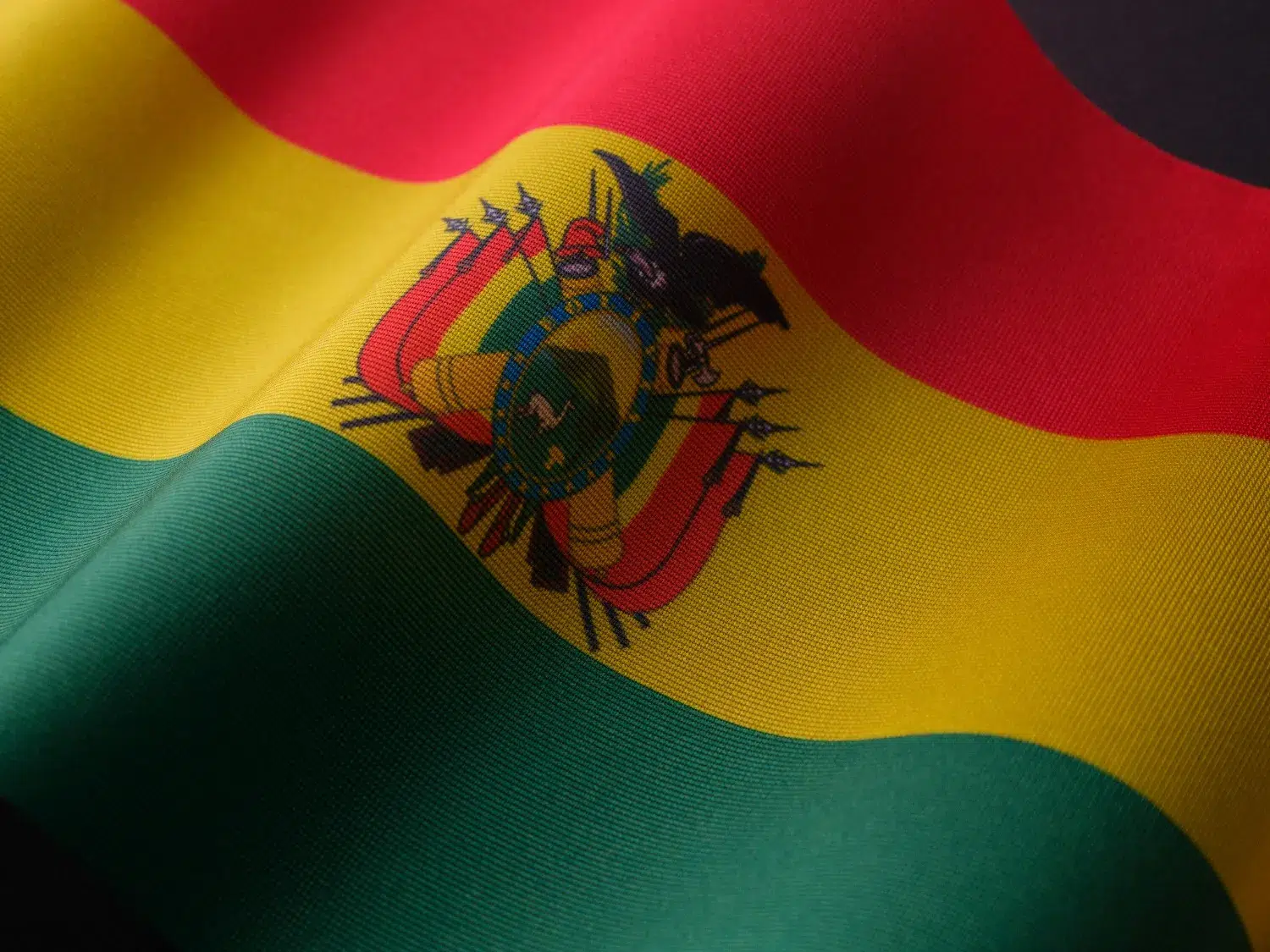 Gros plan sur le drapeau de la Bolivie aux couleurs rouge, jaune et vert avec les armoiries nationales, symbole fort de l’identité bolivienne.