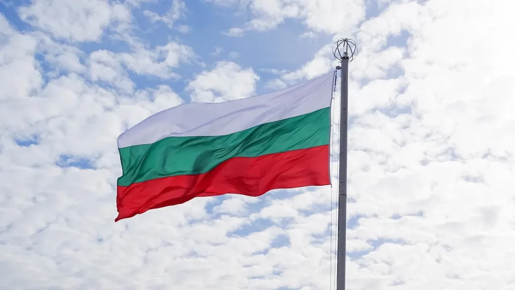 Drapeau bulgare flottant au vent devant un ciel nuageux, représentant les couleurs nationales de la Bulgarie : blanc, vert et rouge.