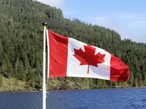 Drapeau du Canada flottant au bord d’un lac entouré de forêts, symbole pour vivre au Canada