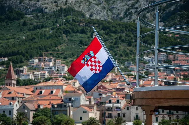 Drapeau croate accroché à un balcon surplombant une ville typique de Croatie avec toits rouges et paysage montagneux.
