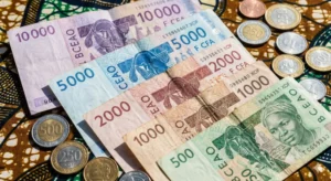 Billets et pièces en francs CFA XOF étalés sur un tissu traditionnel, représentant clairement la monnaie du Bénin.